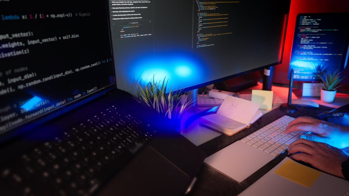 Programmer writing code remote night workspace with multiple screens, RGB lighting and organized modern desk